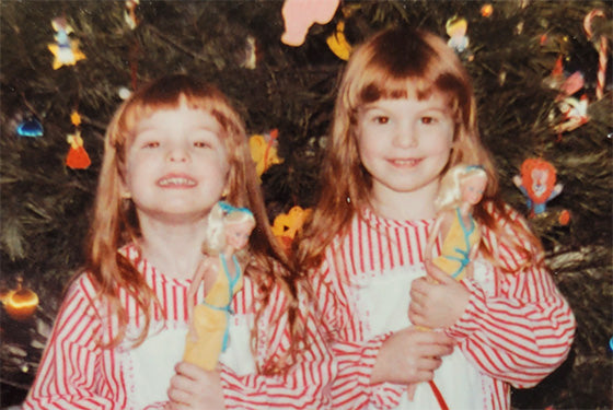 christy johnson and her twin sister as kids holding barbies in front of a christmas tree